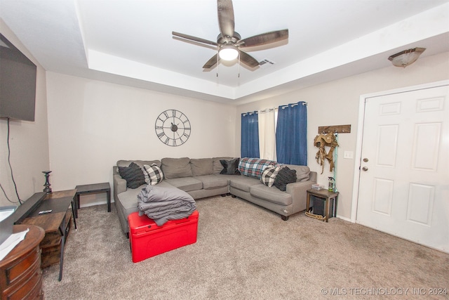 living room with ceiling fan, carpet floors, and a tray ceiling