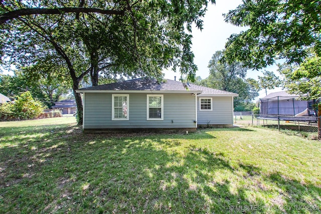 rear view of property featuring a trampoline and a lawn