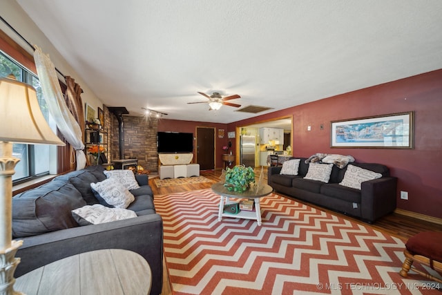 living room featuring ceiling fan, a textured ceiling, light wood-type flooring, and a wood stove