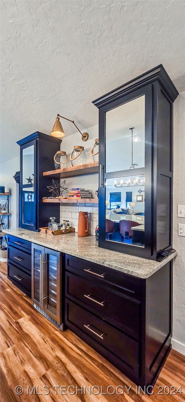 bar with hardwood / wood-style floors, decorative backsplash, light stone countertops, a textured ceiling, and beverage cooler