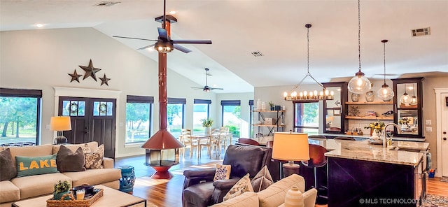 living room with ceiling fan with notable chandelier, light wood-type flooring, and high vaulted ceiling