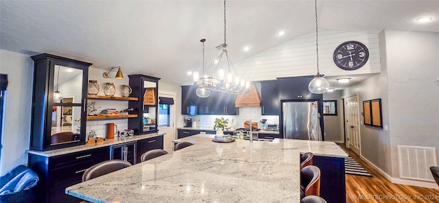 kitchen featuring stainless steel fridge, a center island with sink, decorative light fixtures, and a breakfast bar area