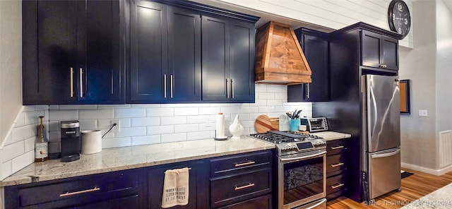 kitchen with light stone countertops, appliances with stainless steel finishes, tasteful backsplash, custom exhaust hood, and hardwood / wood-style floors