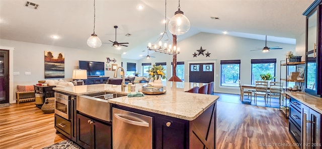 kitchen with hardwood / wood-style floors, decorative light fixtures, stainless steel microwave, and an island with sink