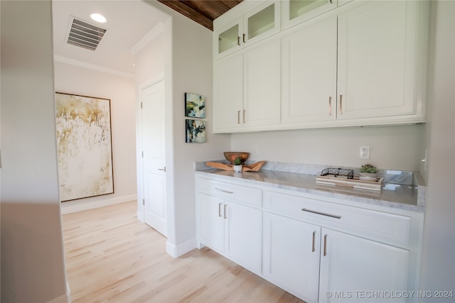 kitchen with white cabinets, beam ceiling, light hardwood / wood-style flooring, crown molding, and light stone countertops