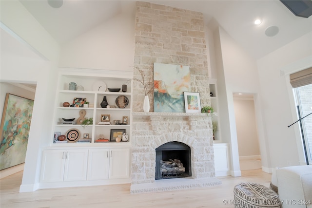 living room with a stone fireplace, light hardwood / wood-style flooring, built in features, and high vaulted ceiling