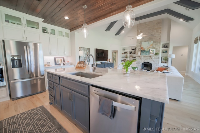 kitchen featuring pendant lighting, sink, a stone fireplace, white cabinetry, and appliances with stainless steel finishes