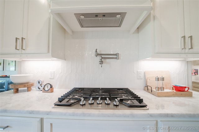 kitchen with stainless steel gas stovetop, white cabinets, and light stone counters