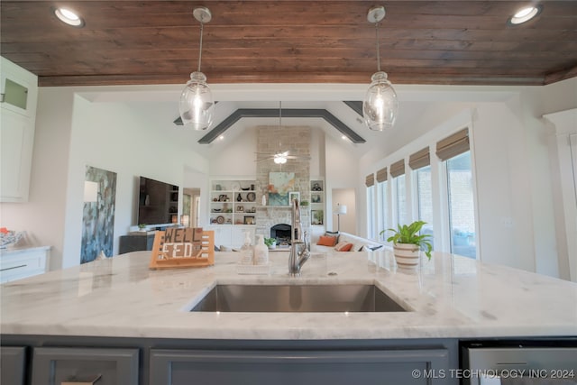 kitchen featuring a fireplace, lofted ceiling, pendant lighting, and light stone counters