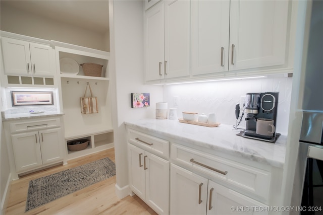 kitchen with light stone countertops, light hardwood / wood-style flooring, stainless steel oven, and white cabinetry