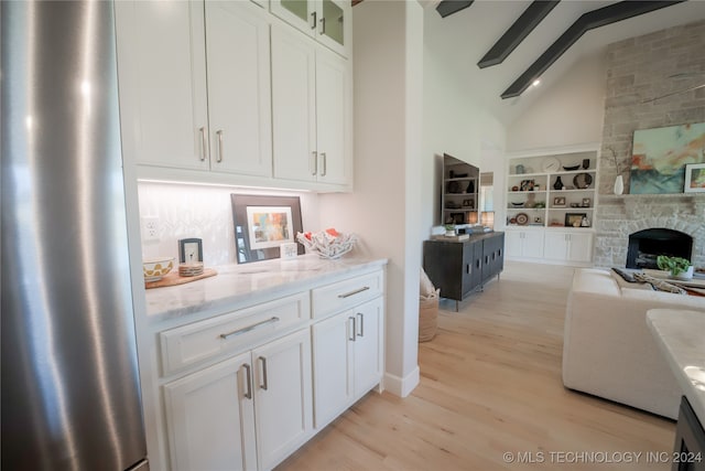 kitchen with lofted ceiling with beams, light hardwood / wood-style floors, white cabinetry, a fireplace, and light stone countertops