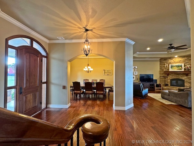 entryway featuring ceiling fan with notable chandelier, a stone fireplace, ornamental molding, and dark hardwood / wood-style flooring