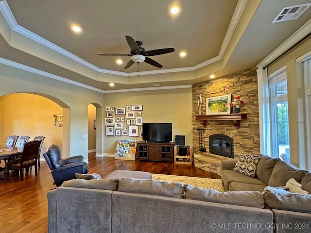 living room featuring wood-type flooring, a stone fireplace, crown molding, and ceiling fan