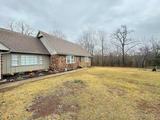 view of home's exterior with stone siding, a shingled roof, a lawn, and board and batten siding