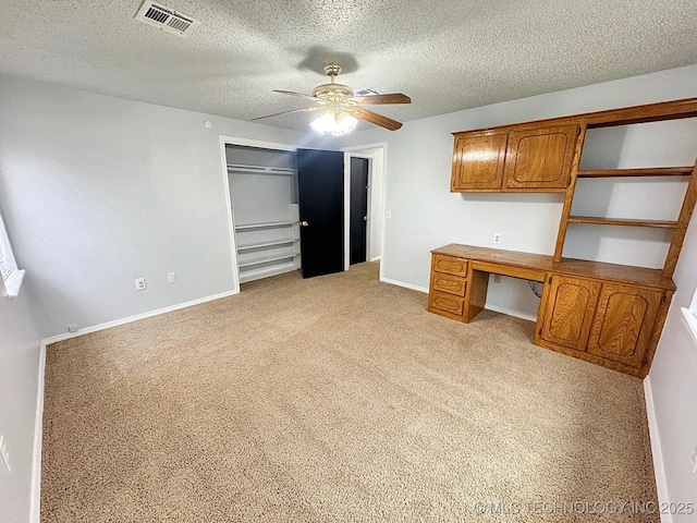 unfurnished office with visible vents, light carpet, ceiling fan, built in study area, and baseboards