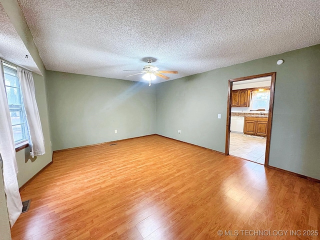 unfurnished room featuring light wood-type flooring, ceiling fan, visible vents, and a textured ceiling