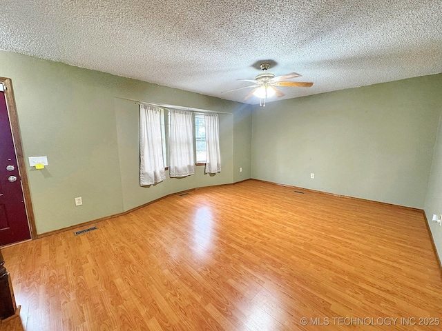 spare room with light wood-style flooring, a textured ceiling, visible vents, and a ceiling fan