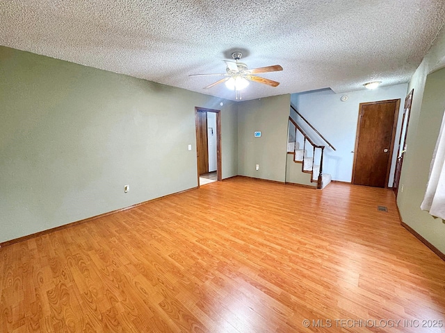 empty room featuring baseboards, a ceiling fan, stairway, a textured ceiling, and light wood-type flooring