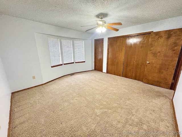 unfurnished bedroom featuring a textured ceiling, carpet floors, ceiling fan, and two closets