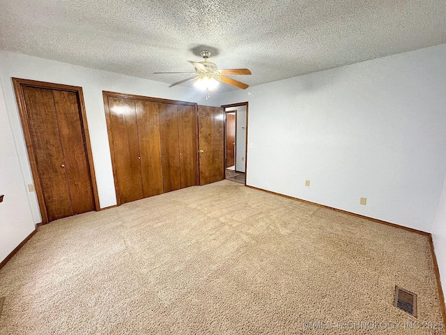 unfurnished bedroom featuring carpet floors, visible vents, a textured ceiling, and multiple closets