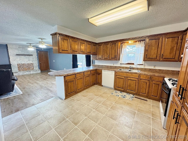 kitchen with brown cabinetry, dishwasher, gas range, a peninsula, and a sink