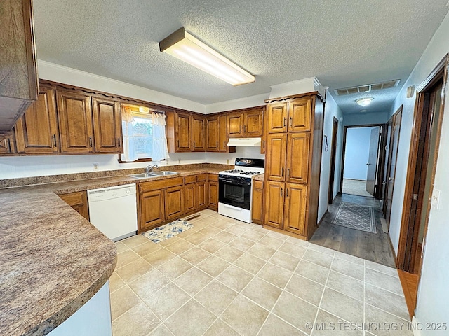 kitchen featuring white dishwasher, brown cabinets, a sink, and gas stove