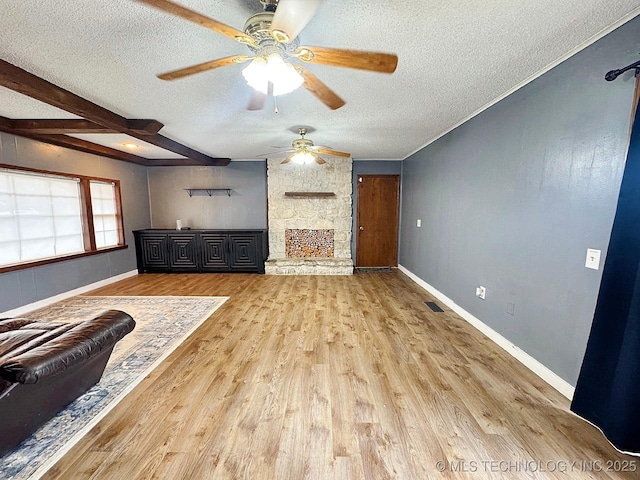 unfurnished living room with a textured ceiling, a stone fireplace, baseboards, beam ceiling, and light wood finished floors