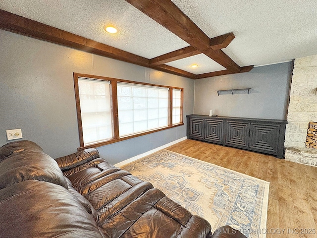 living area with a textured ceiling, coffered ceiling, baseboards, light wood-style floors, and beamed ceiling