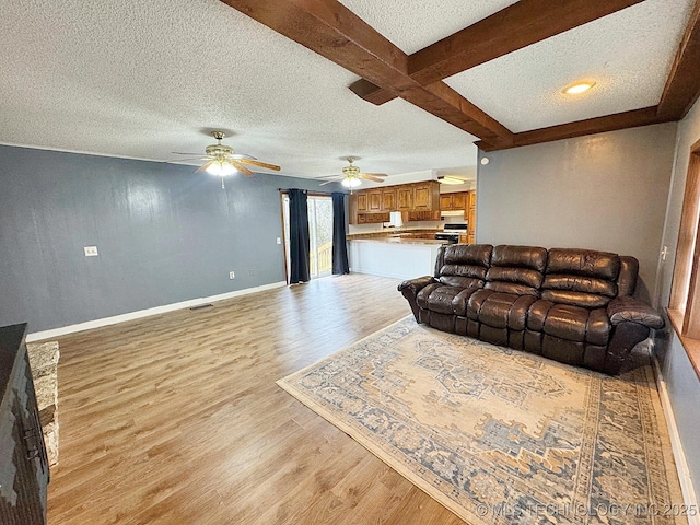 living room with beam ceiling, light wood finished floors, a ceiling fan, a textured ceiling, and baseboards