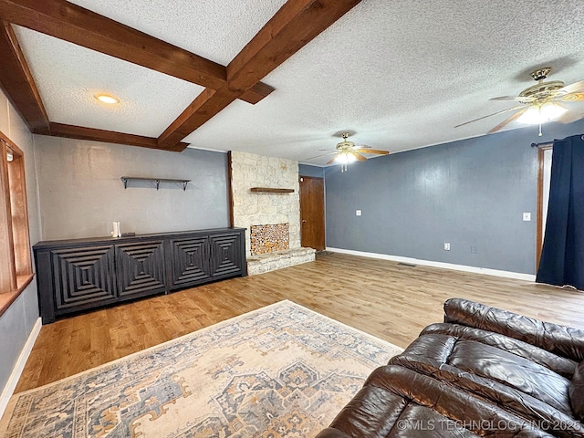 living area featuring a textured ceiling, a fireplace, a ceiling fan, light wood-style floors, and beamed ceiling