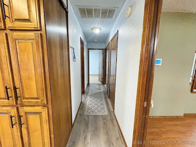 hall featuring visible vents, light wood-style flooring, baseboards, and a textured ceiling