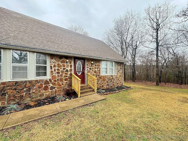 single story home with stone siding, a shingled roof, and a front yard