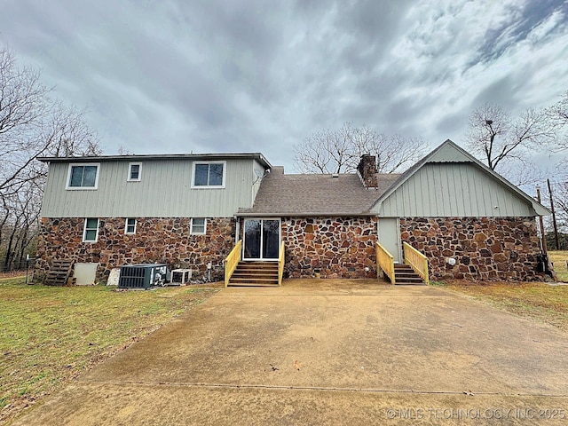 rear view of property featuring brick siding, a yard, a chimney, central AC unit, and entry steps