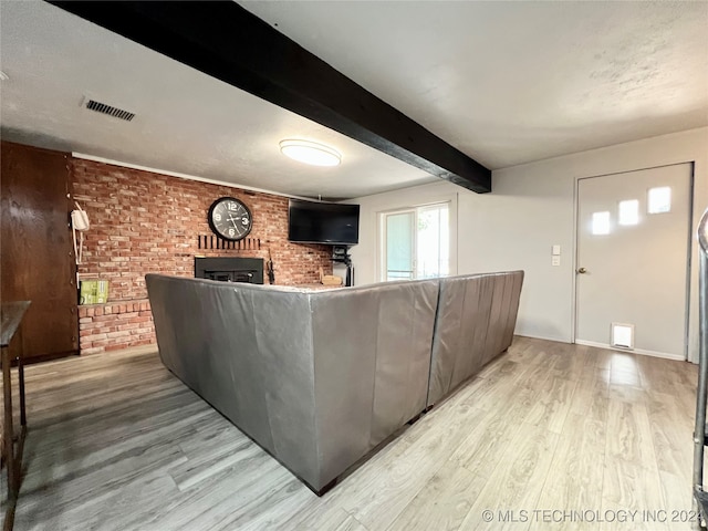 unfurnished living room with light hardwood / wood-style flooring, a brick fireplace, beam ceiling, and brick wall