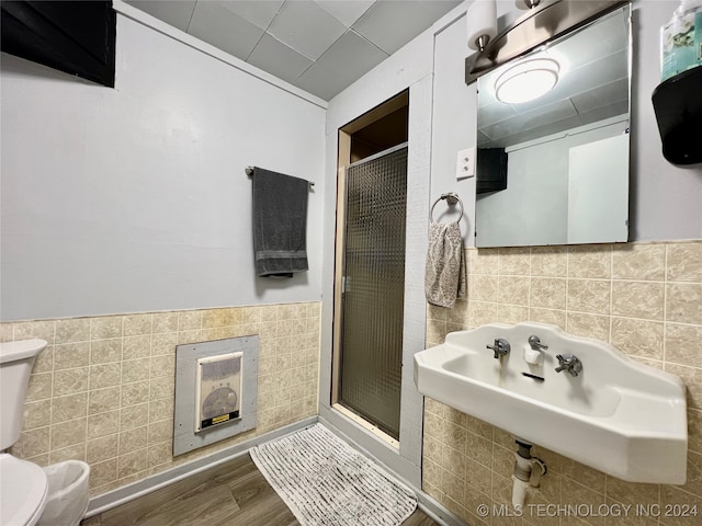 bathroom featuring tile walls, a shower with door, toilet, and wood-type flooring