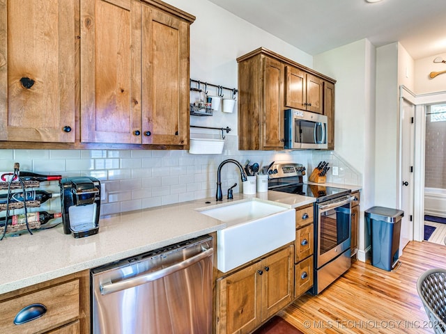 kitchen featuring sink, light hardwood / wood-style flooring, appliances with stainless steel finishes, light stone counters, and decorative backsplash