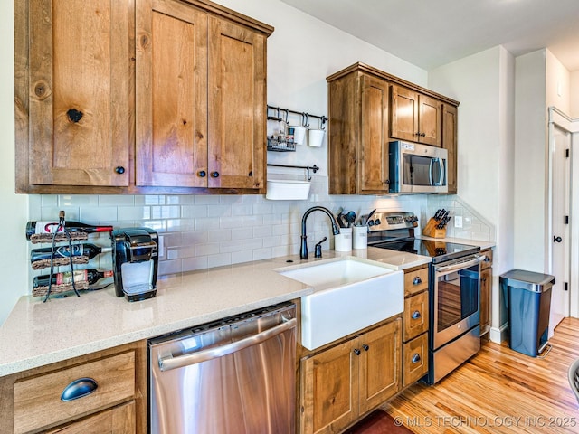 kitchen featuring sink, light hardwood / wood-style flooring, backsplash, stainless steel appliances, and light stone counters