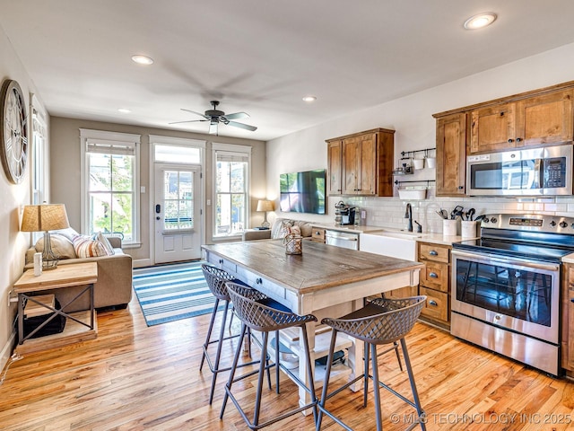 kitchen featuring sink, light hardwood / wood-style flooring, ceiling fan, stainless steel appliances, and tasteful backsplash