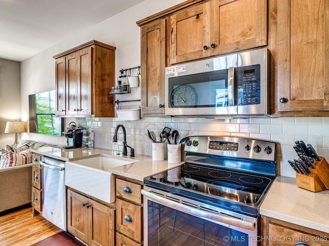 kitchen featuring stainless steel appliances, sink, light hardwood / wood-style flooring, and backsplash