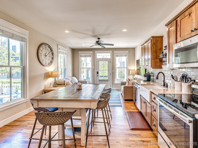 kitchen featuring appliances with stainless steel finishes, a wealth of natural light, sink, decorative backsplash, and light wood-type flooring