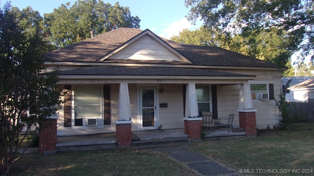 bungalow-style home with cooling unit, a porch, and a front lawn