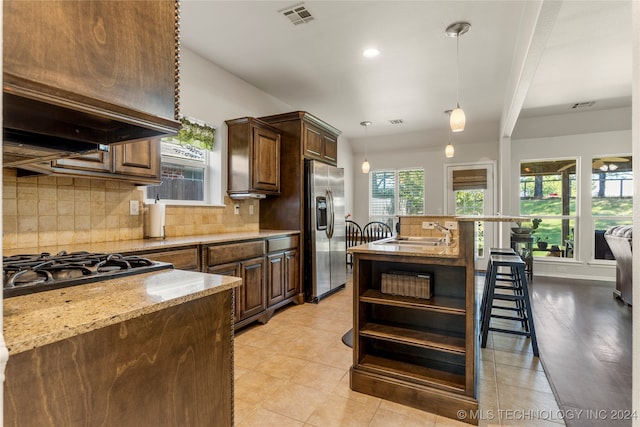 kitchen with tasteful backsplash, hanging light fixtures, light stone counters, appliances with stainless steel finishes, and sink