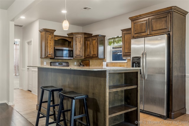 kitchen with tasteful backsplash, a breakfast bar area, light stone countertops, light hardwood / wood-style floors, and stainless steel appliances