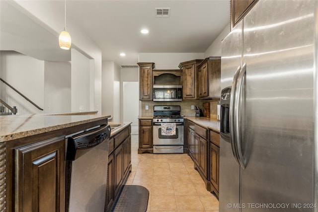 kitchen featuring dark brown cabinets, backsplash, appliances with stainless steel finishes, pendant lighting, and light stone counters