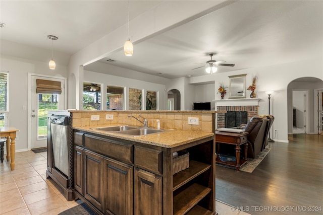 kitchen with a kitchen island with sink, sink, a brick fireplace, light wood-type flooring, and tasteful backsplash