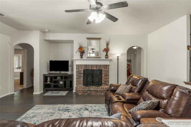 living room featuring dark hardwood / wood-style floors, ceiling fan, and a brick fireplace