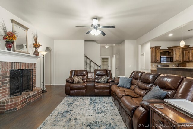 living room with a brick fireplace, dark hardwood / wood-style floors, and ceiling fan