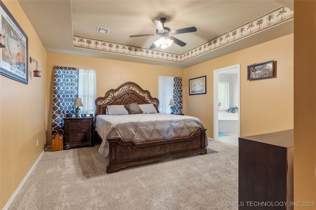 bedroom featuring ceiling fan, light colored carpet, a tray ceiling, and ensuite bath