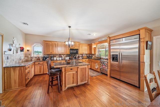 kitchen featuring an island with sink, backsplash, appliances with stainless steel finishes, and hanging light fixtures