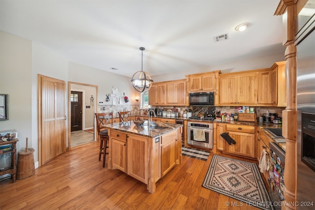 kitchen with pendant lighting, light hardwood / wood-style floors, a kitchen island with sink, and stainless steel oven